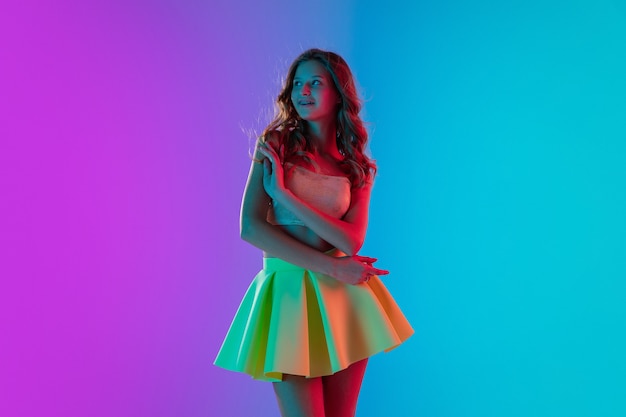 Beautiful seductive girl in fashionable yellow skirt on gradient pink-blue neon wall