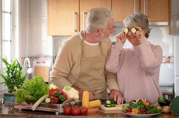野菜を準備しながらズッキーニの2つのスライスとキッチンで笑っている美しい年配のカップル