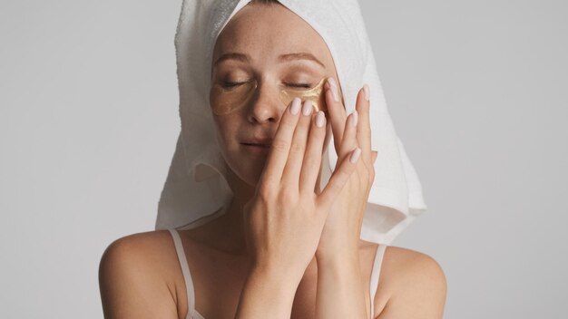 白い背景で隔離の目のパッチを適用する頭にタオルで美しい官能的な女性。美容コンセプト