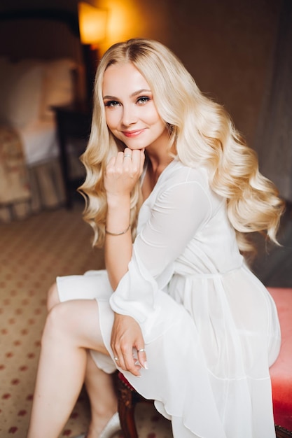 Beautiful and sensuality blondie bride sitting in bedroom dreaming with closed eyes Young and sexy woman with long curly hair and perfect make up wearing in lace lingerie Morning before wedding