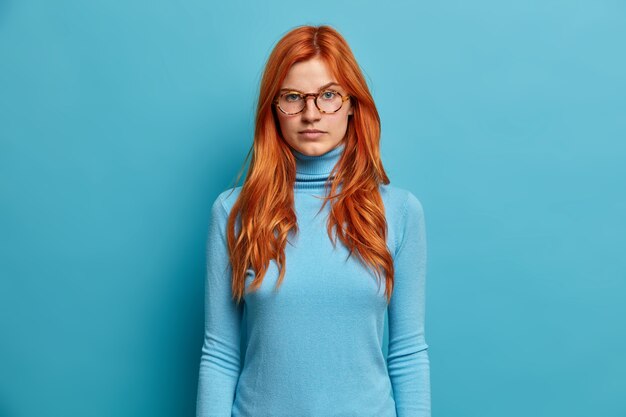 美しい真面目な赤毛のミレニアル世代の女性は、落ち着いた自信を持って直接見つめ、カジュアルな服を着た光学メガネをかけているものを注意深く聞きます。