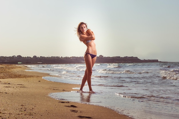 Красивая сексуальная блондинка в купальнике позирует на пляже на песке