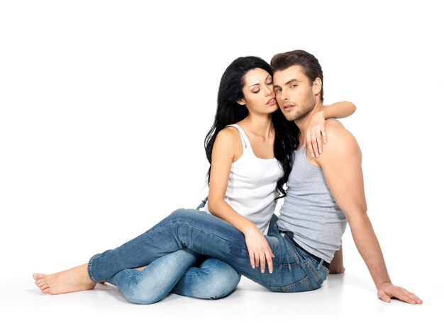 Beautiful sexy couple in love on white wall dressed in blue jeanse and white undershirt