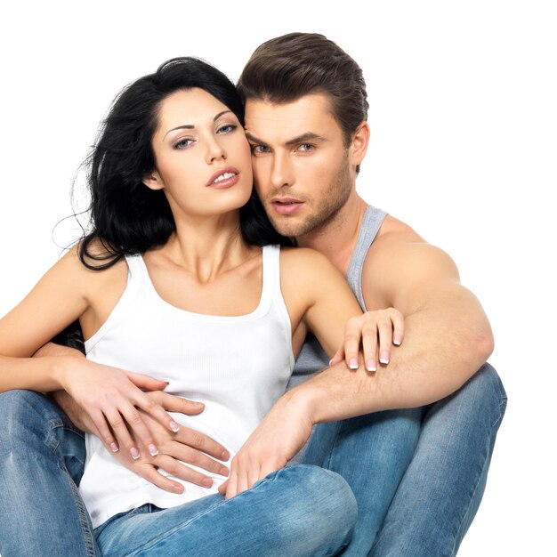 Beautiful sexy couple in love on white wall dressed in blue jeanse and white undershirt