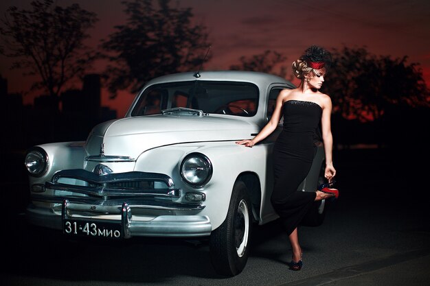 beautiful sexy fashion blond girl model with bright makeup and curly hairstyle in retro style sitting in old car