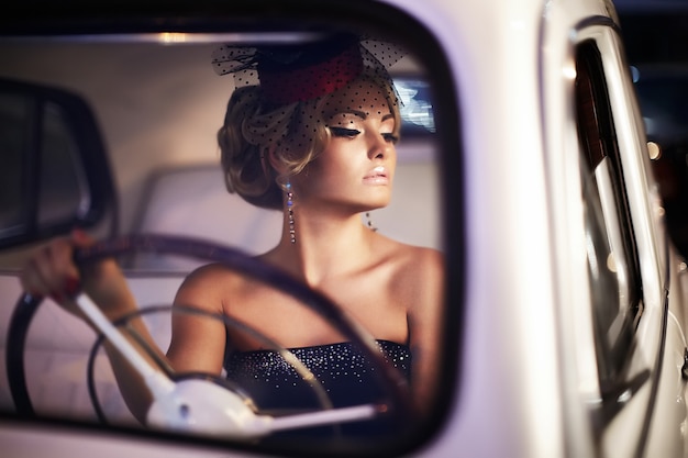 beautiful sexy fashion blond girl model with bright makeup and curly hairstyle in retro style sitting in old car