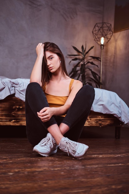 Beautiful sexy girl is sitting on the floor at her bedroom. She has casual style and long hair.