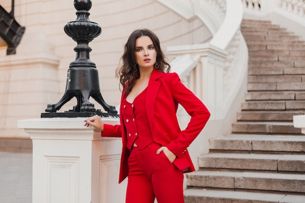 街の通りを歩く赤いスーツの美しいセクシーでリッチなビジネススタイルの女性、春夏のファッショントレンド