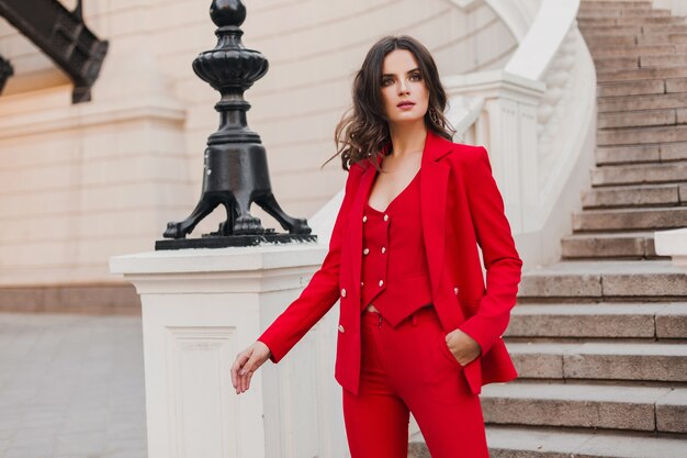 Красивая сексуальная богатая деловая женщина в красном костюме гуляет по городской улице, весенне-летняя мода