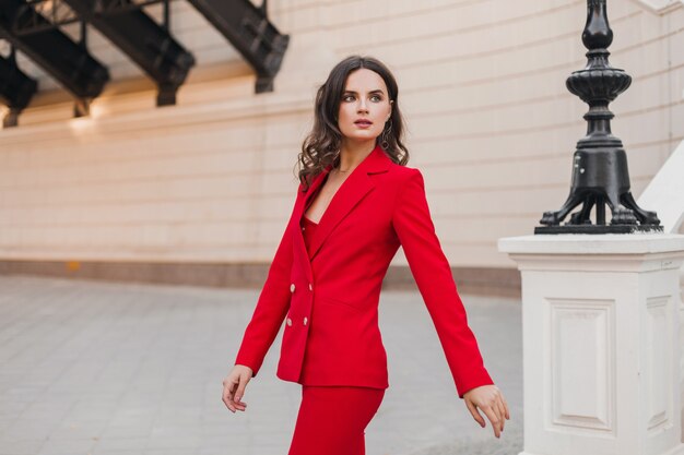 Красивая сексуальная богатая деловая женщина в красном костюме гуляет по городской улице, весенне-летняя мода