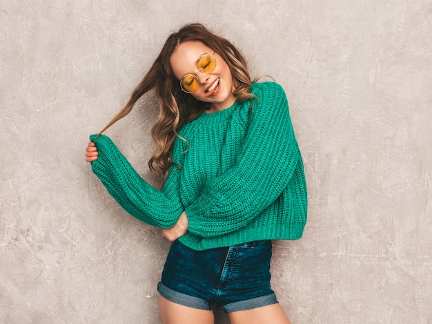 Beautiful sexy smiling gorgeous girl in green trendy sweater. woman posing in round sunglasses. model having fun and showing her tongue