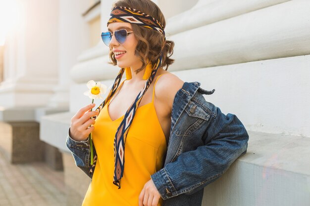 Красивая сексуальная стильная женщина в желтом стильном платье в джинсовой куртке, модный наряд, модный тренд весна-лето, солнечные, синие солнцезащитные очки, уличная мода, стиль хипстера, модные аксессуары