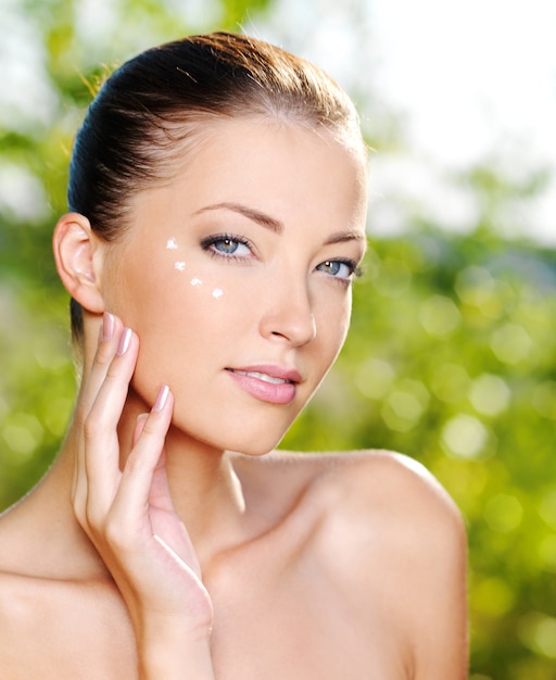 Beautiful sexy woman applying cosmetic cream on skin near eyes - Outdoors