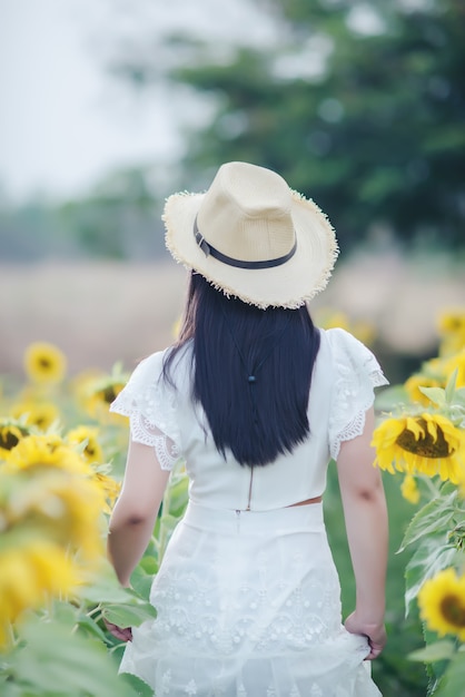 Bella donna sexy in un abito bianco che cammina su un campo di girasoli