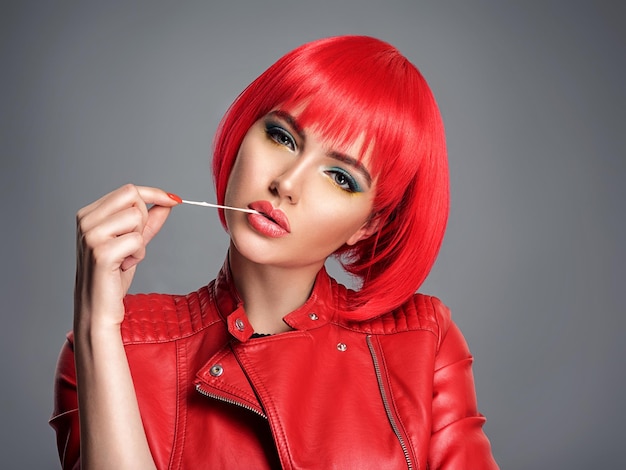 Beautiful sexy woman with bright red bob hairstyle. Fashion  model. Sensual  gorgeous girl in a leather jacket. Stunning face of a pretty lady. Bright girl stretches gum
