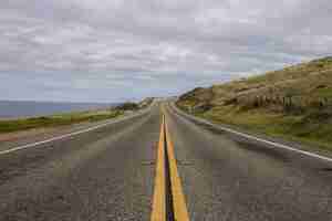 Free photo beautiful shot of an asphalt road surrounded by mountains and the ocean on a cloudy day