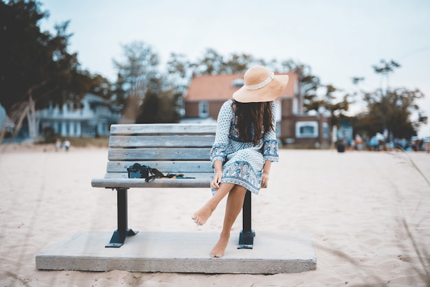 Foto gratuita bello colpo di una femmina scalza che si siede su un banco alla spiaggia con uno sfocato