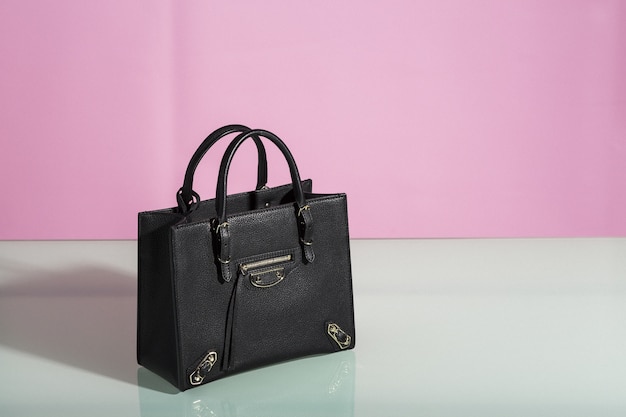 Free photo beautiful shot of a black purse on a white table with a pink