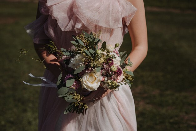 Bello colpo di un vestito da sposa d'uso da sposa che tiene un mazzo del fiore