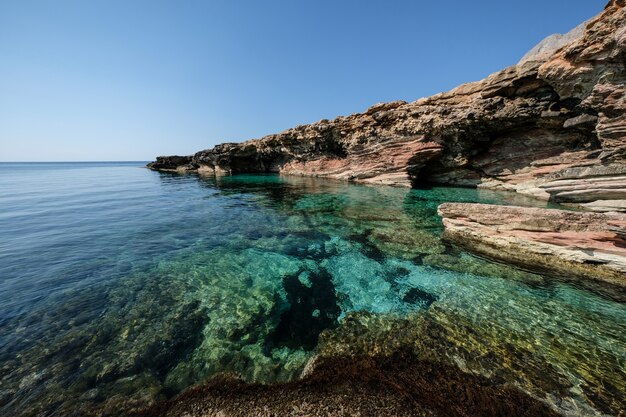 Beautiful shot of clear water near a rocky cliff on a sunny day