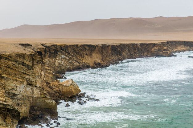 Beautiful shot of a cliff near the sea with mountains in the distance