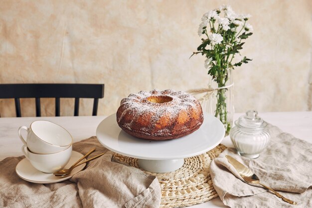 Красивый снимок вкусного кольцевого торта на белой тарелке и белый цветок рядом с ним