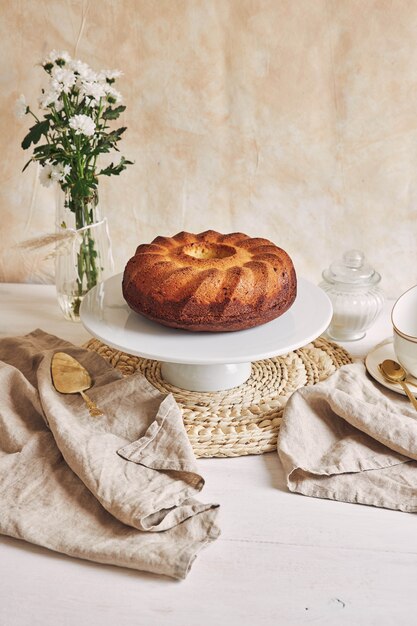 Красивый снимок вкусного кольцевого торта на белой тарелке и белый цветок рядом с ним