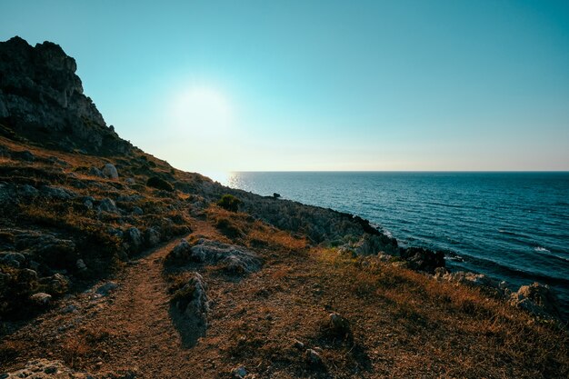 Beautiful shot of dry grass hill and cliff near the sea with clear blue sky