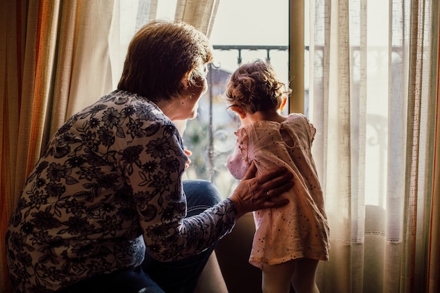 Free photo beautiful shot of an elderly female and a baby girl looking through a window