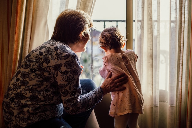 Beautiful shot of an elderly female and a baby girl looking through a window