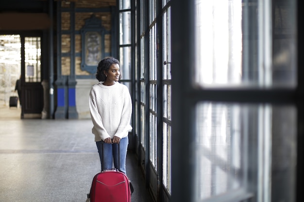 Free photo beautiful shot of a female on the white long sleeve with red luggage while looking at a window