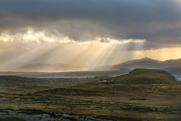 Beautiful shot of the fields and mountains with sun rays shining through clouds