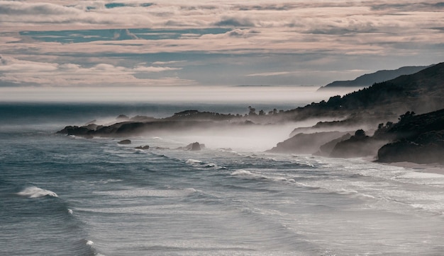 Foto gratuita bellissimo colpo di montagne nebbiose e onde del mare nell'oceano