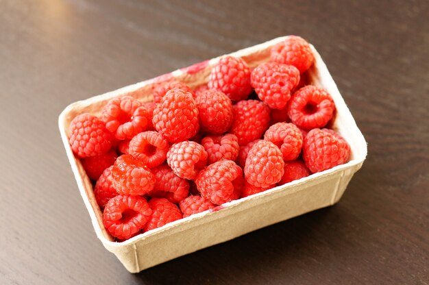 Beautiful shot of fresh raspberries in a plastic plate on the wooden table