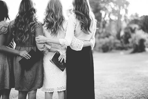 Beautiful shot from behind of females with their arms around each other while holding the bible