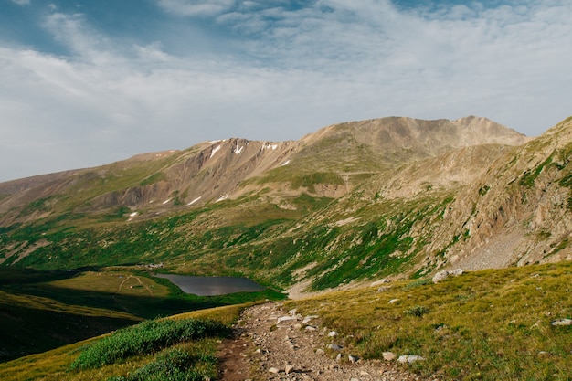 Beautiful shot of green hills near mountains with a pond in the distance  under a cloudy sky