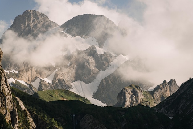 Beautiful shot of green mountains covered with white clouds in a clear blue sky