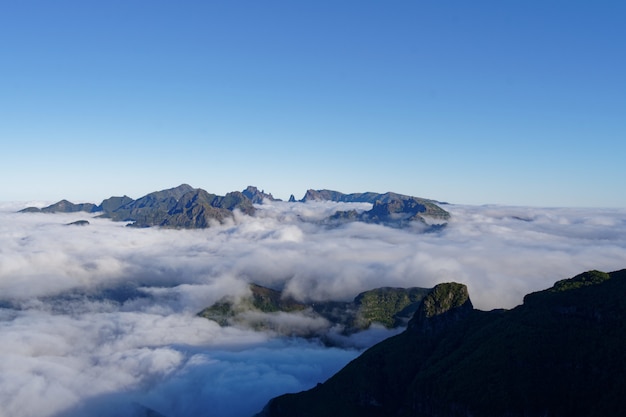 Beautiful shot of green mountains and hills covered in white clouds in a clear sky