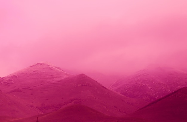 Beautiful shot of the hills covered in fog in a pink-tinted color