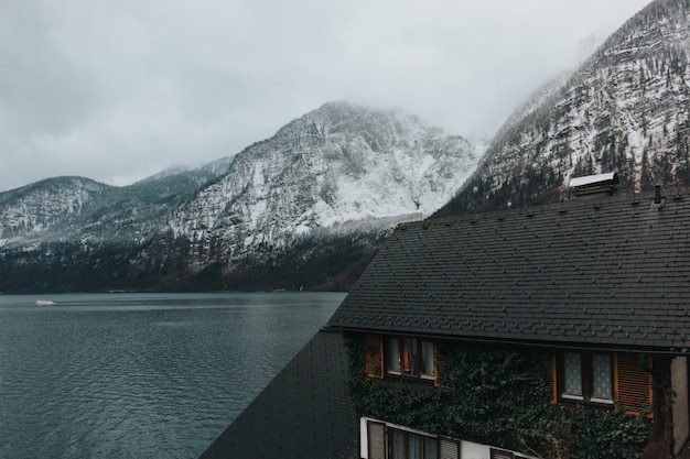 Красивый снимок дома возле озера и серых гор, покрытых снегом в дневное время