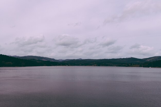 Beautiful shot of a lake with hills on the horizon and cloudy sky