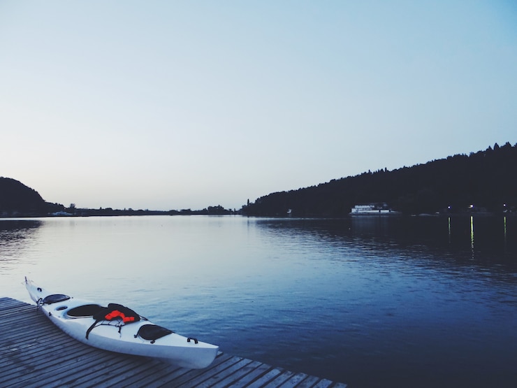 Free Photo beautiful shot of a lake with a white kayak on a brown wooden dock