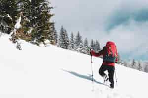 Foto gratuita bellissimo scatto di un escursionista maschio con uno zaino da viaggio rosso che fa un'escursione su una montagna innevata in inverno