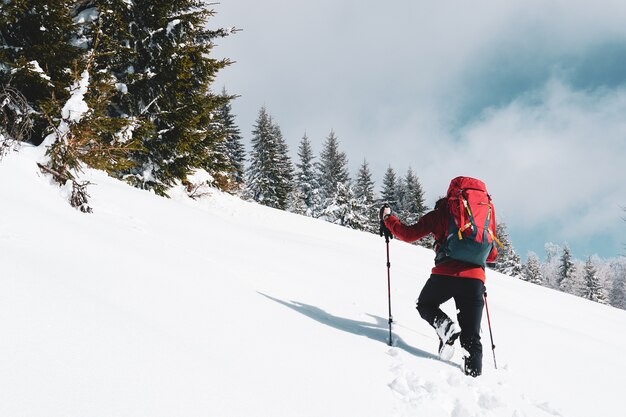 Beautiful shot of a male hiker with a red travel backpack hiking up a snowy mountain in winter