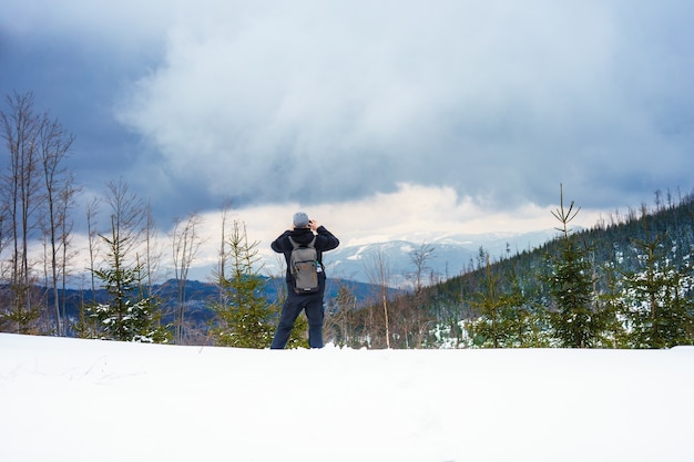 雪に覆われた森林に覆われた山々の写真を撮る男の美しいショット