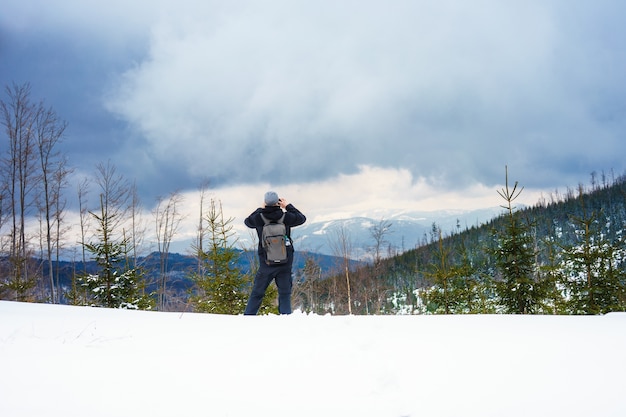 Beautiful shot of a man taking a picture of snowy forested mountains