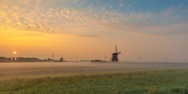 Beautiful shot of mills in the field with the sun rising in the