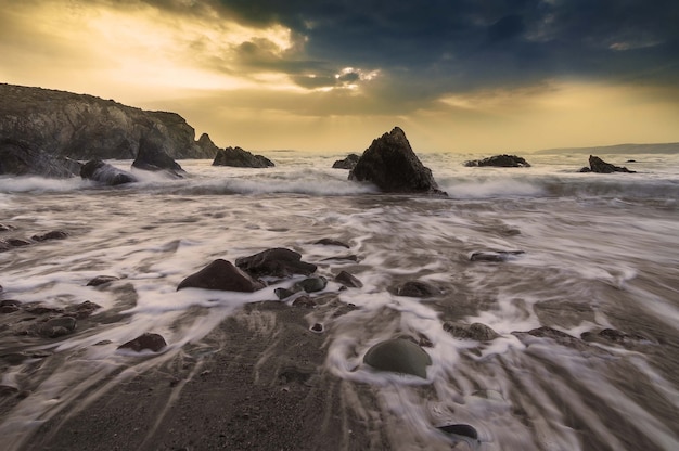 Beautiful shot of the ocean waves crashing on the rocky shore during sunset