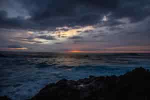 無料写真 夕暮れ時の曇り空の下の岩の近くの海の波の美しいショット