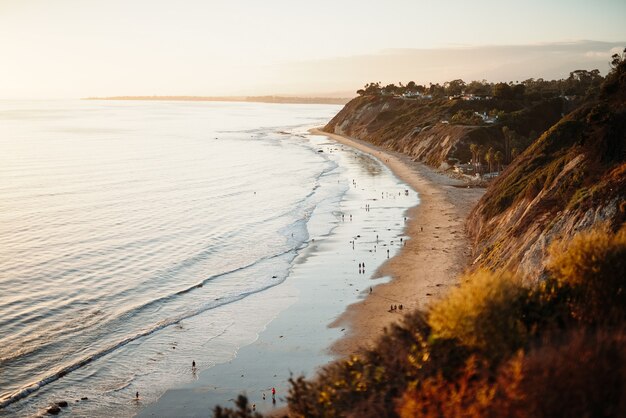 Beautiful shot of people walking in a wild seashore next to low hills